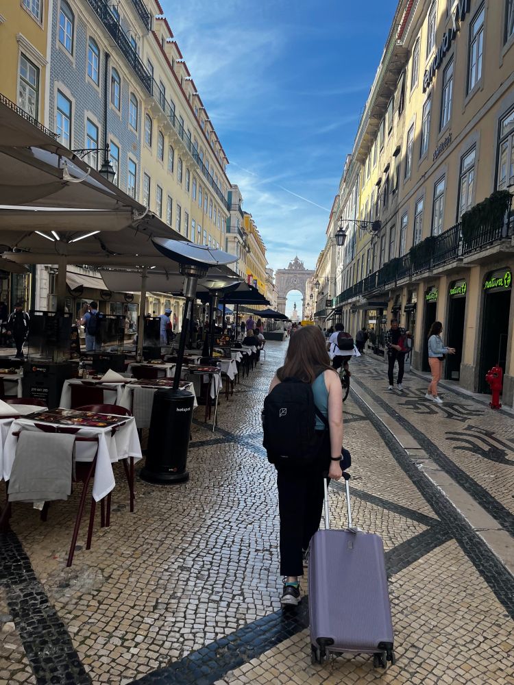 Woman walking through Lisbon street with a purple suitcase in the morning