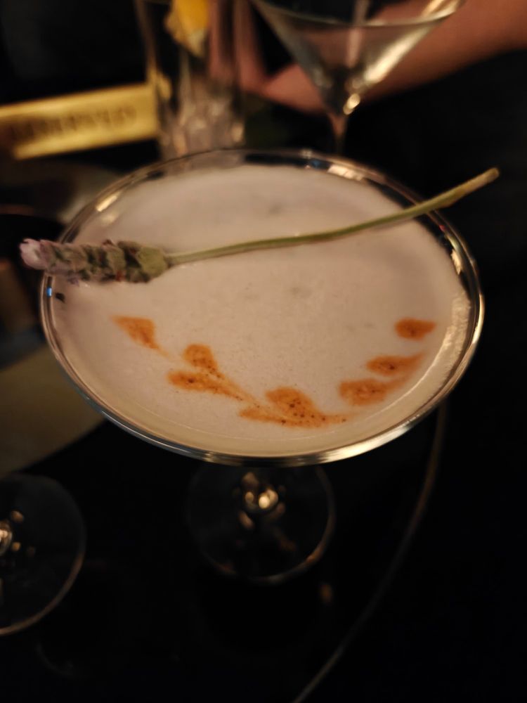 top view of the flight club drink. there are red hearts drawn in the foam, and a fresh sprig of lavender resting across the rim of the glass