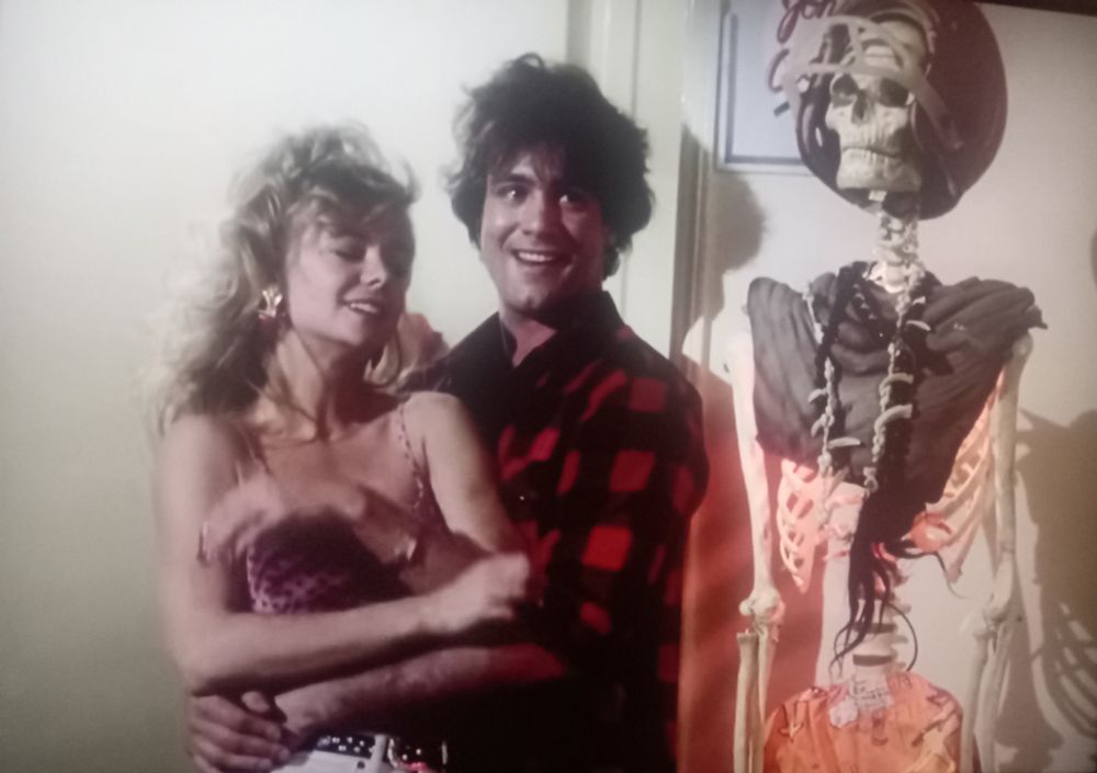 Shot from Slaughterhouse Rock film with a man in a flannel shirt standing between a woman and a skeleton.