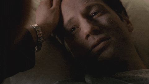 Gif from the X Files. Mulder lies in a hospital bed looking pale. Scully is very emotionally looking at him, tear tracks on her cheeks, and tenderly stroking his forehead and hair. 