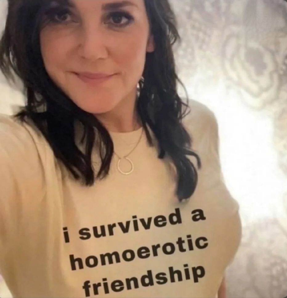 woman smirking in shirt that reads "i survived a homoerotic friendship" 
