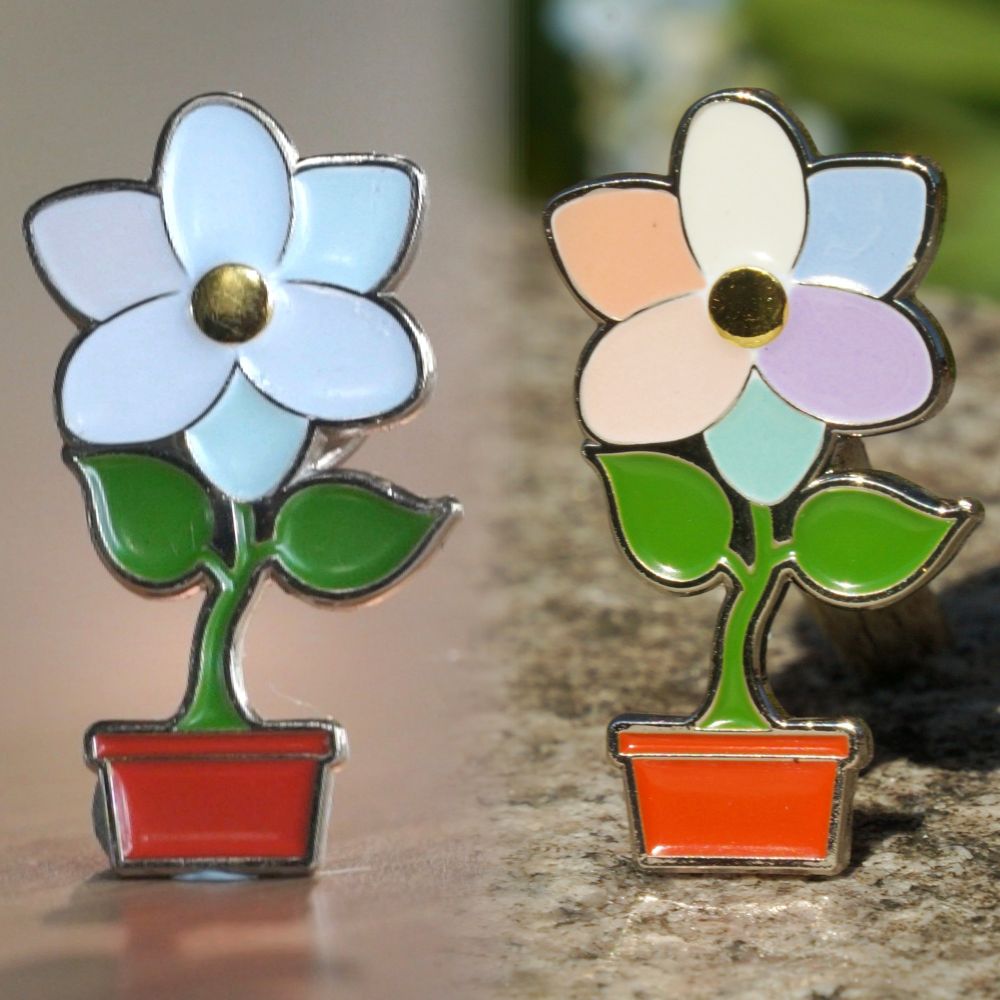 An enamel pin in the shape of a flower with six petals, two leaves, and a plant pot. It is shown twice to illustrate colour change. On the left, the petals are white and it is indoors. On the right, the petals are pastel shades of the LGBTQ+ pride flag and it is outdoors in sunshine.