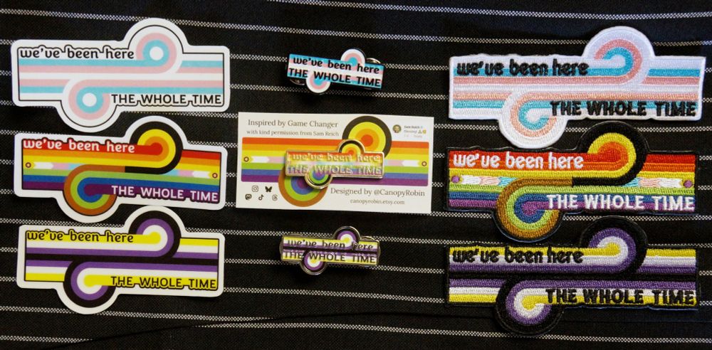 Stickers, enamel pins, and embroidered patches in trans pride, intersex inclusive progress pride, and non-binary pride colours. The shape of the design is the loop-de-loop emblem of the Dropout show Game Changer, and each design has the words "we've been here the whole time" written on it