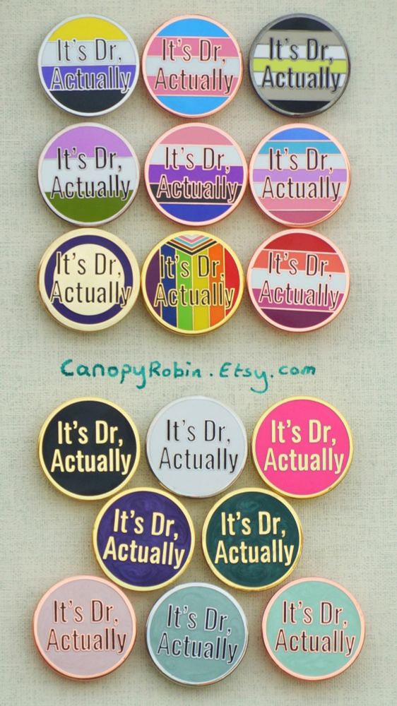 A collection of circular hard enamel pins which say "It's Dr, Actually". The backgrounds of the pins are in the style of the nonbinary, trans, agender, genderqueer, genderfluid, bigender, intersex, lesbian, and progress pride flags. There are also flagless backgrounds in black, white, hot pink, pearlescent purple, pearlescent dark green, pearlescent pink, pearlescent light blue, and pearlescent light green. A handwritted URL directs you to look up CanopyRobin.Etsy.Com