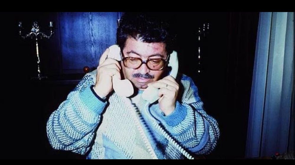 Former Turkish president and prime minister Turgut Özal, in a blue knit sweater, holding two rotary phones to his ears. 