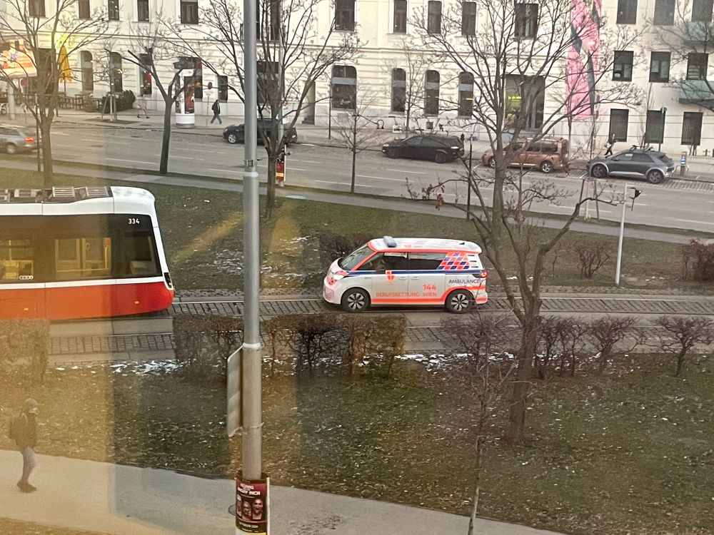 VW iD.Buzz in Lackierung der Wiener Berufsrettung vom 2.OG hinter einer Straßenbahn fotografiert.