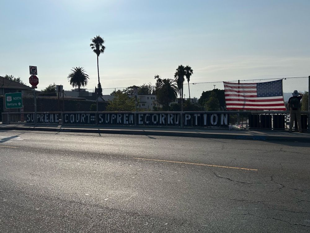 golden hour and the setting sun behind a protest sign that reads supreme court = supreme corruption 