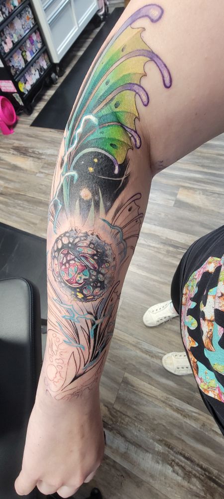 Picture of an arm with a partially finished tattoo. In the center is an arcane anomaly and surrounding it is leaves with electricity through them. 
