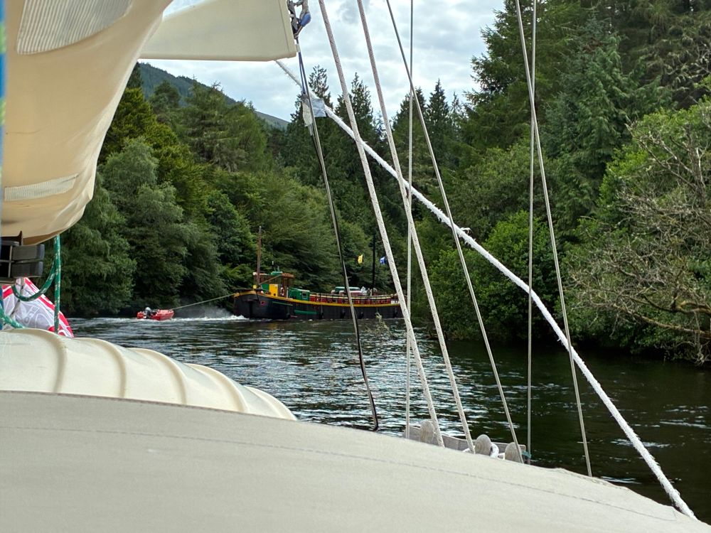 Indigo cruising in a veritable forest path of a canal, between Oich and Lochy. A black and green large river barge turns the corner of the canal ahead of us.