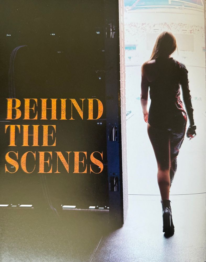A photo from the eras tour book that pictures Taylor swift walking out onto stage from the back with glittery ORANGE lettering that says “behind the scenes”
