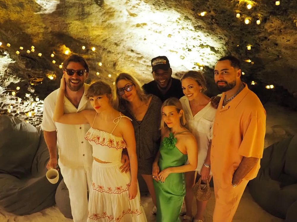 Taylor Swift and Travis Kelce both wearing all white posing with a bunch of friends, one of whom is the blonde Haim sister