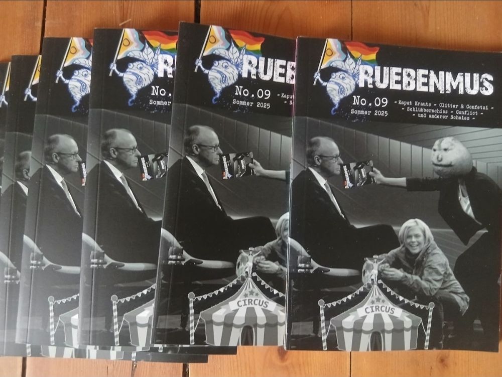 Mehrere Rübenmushefte, Merz bekommt RüMu ins Gesicht, Klöckner präsentiert stolz den Circus mut Jesus am Kreuz.