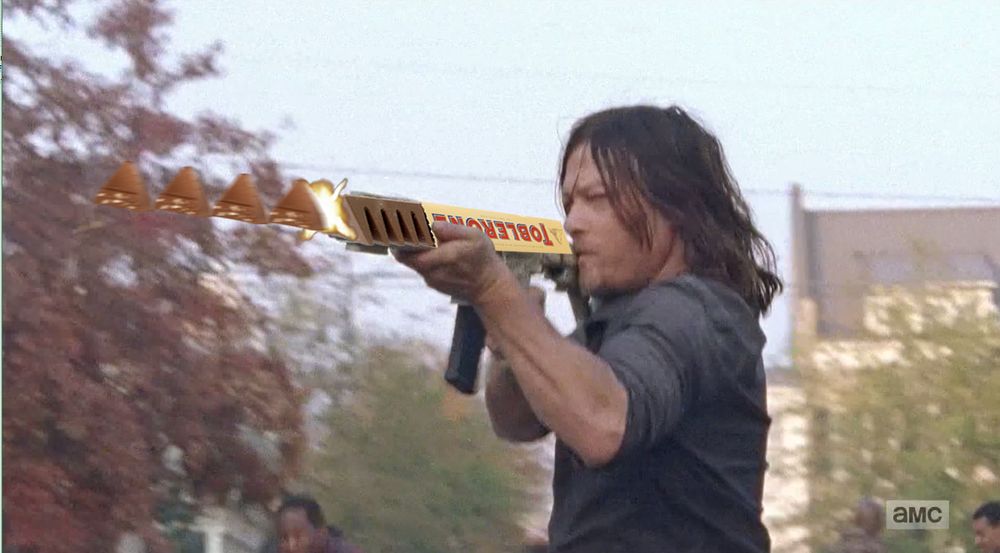 Man shooting machine gun, but the barrel is an upside down Toblerone, with some chocolate visible, and for some reason it's firing rightside up pieces of Toblerone.