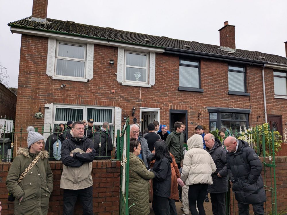 Photo of a crowd of people standing in front of a terraced house.