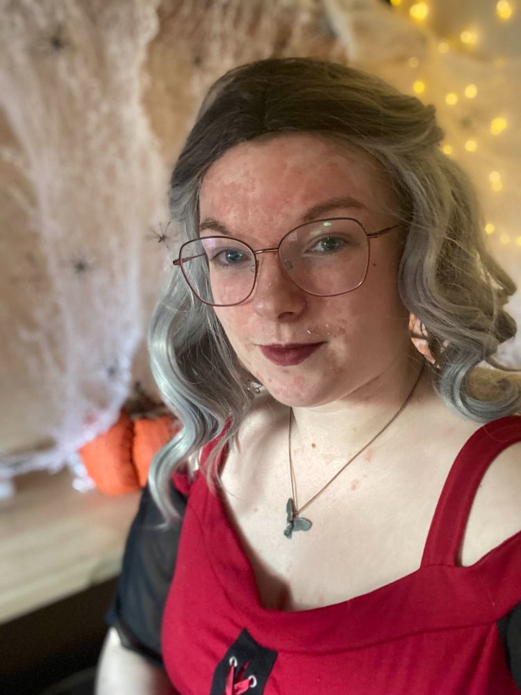 Wonder in a grey wig, witches dress, posing in front of cobwebs, spiders and a pumpkin background.