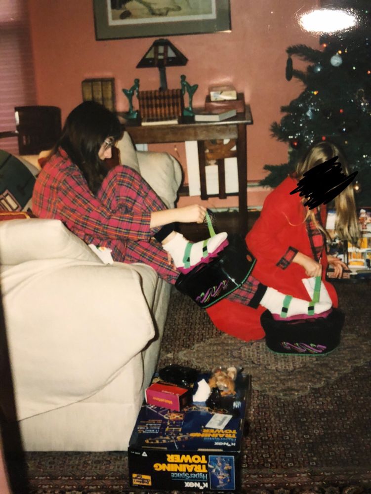 Past me, in her pink plaid pajamas, is sitting on a white couch strapping MOON SHOES to my feet. A sibling in a red robe is behind me