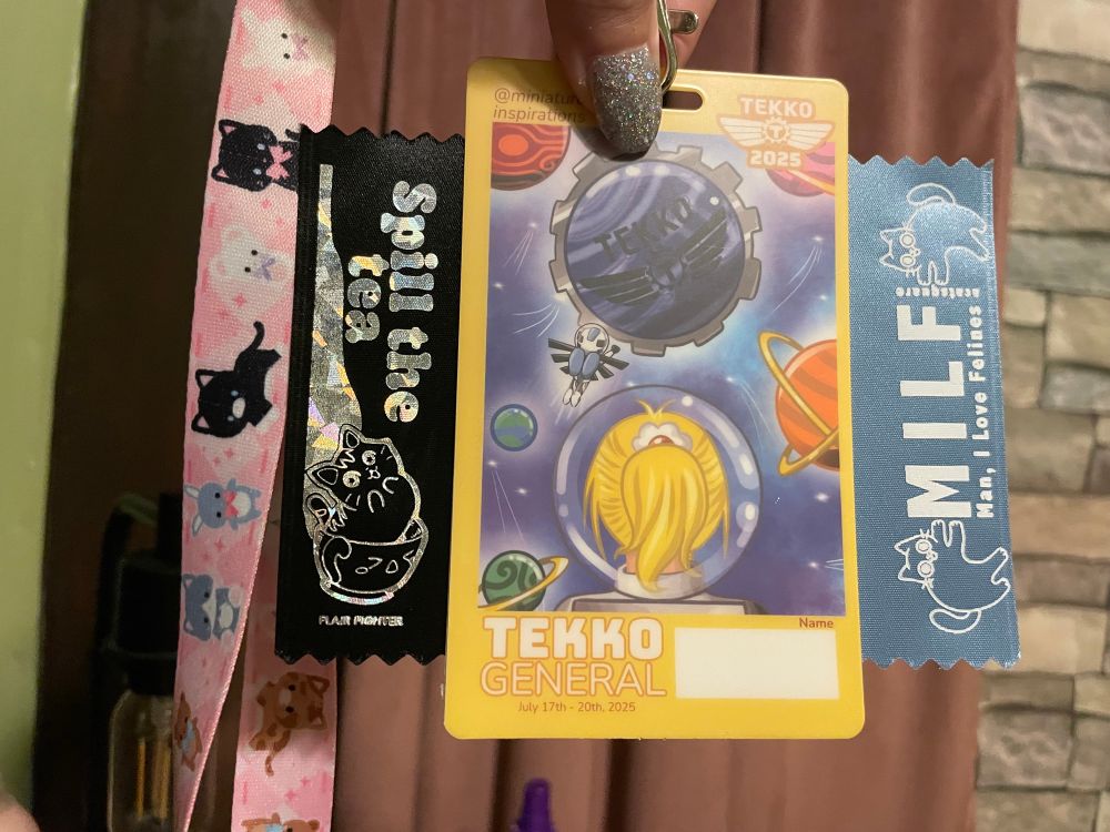 my tekko badge with a cat in a tea cup says spill the tea tag. and a cat tag that says M I L F (milf) “ man, I love felines”