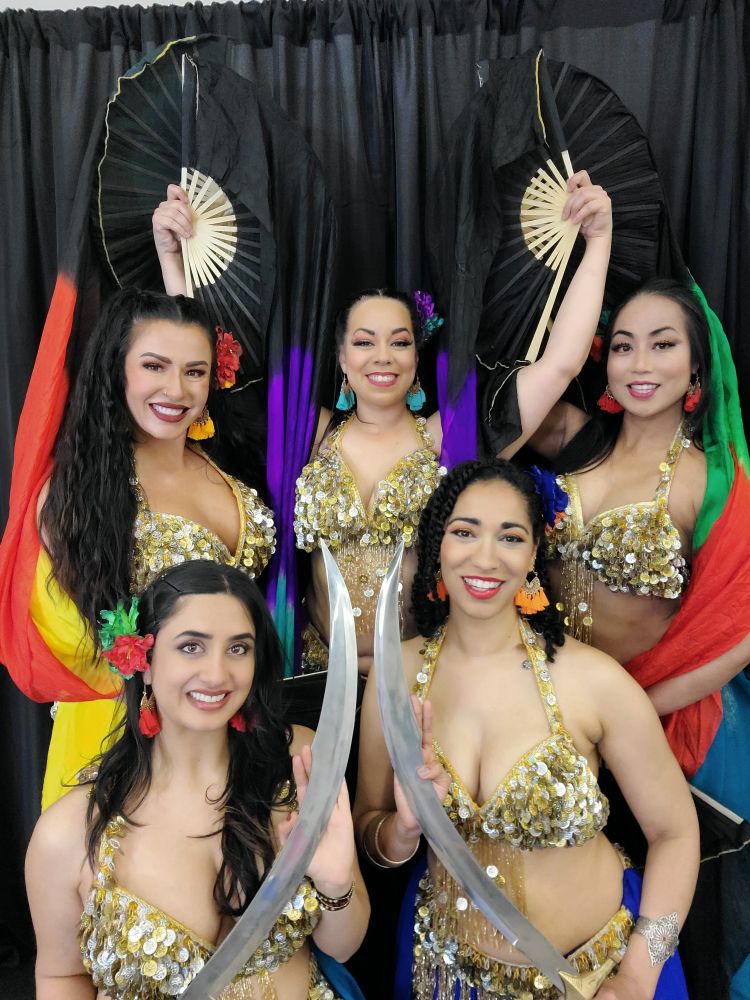Dancers Shef and Mica kneeling in the front row with swords and dancers Dani, Halle and Cici standing behind them with fanveils in front of a black backdrop at The Guild of Middle Eastern Dance's Spring Spectacular at Elision Theater in Crystal, Minnesota. 