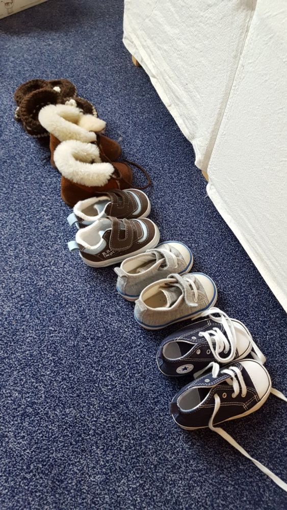 Fünf Paar kleine Kinderschuhe, ordentlich aufgereiht, nebeneinander auf dem Boden. 