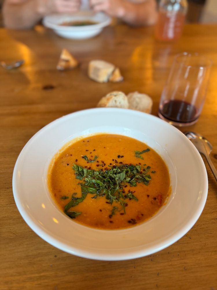 A bowl of delicious creamy tomato lentil soups with bread and wine. 