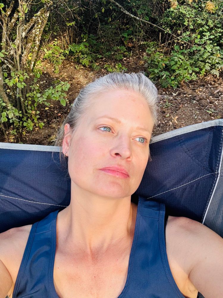 Middle aged grey blonde woman soaking up life at the start of camping vacation. 