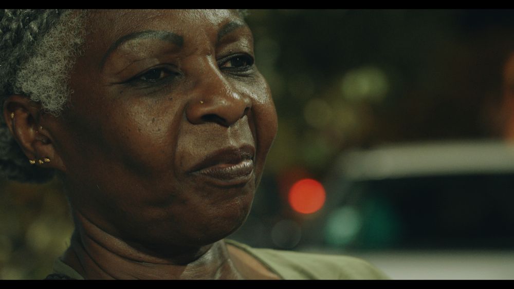 screen du film : une femme guyanaise plutôt âgée, filmée de près, avec un petit sourire et un regard mélancolique, il fait nuit