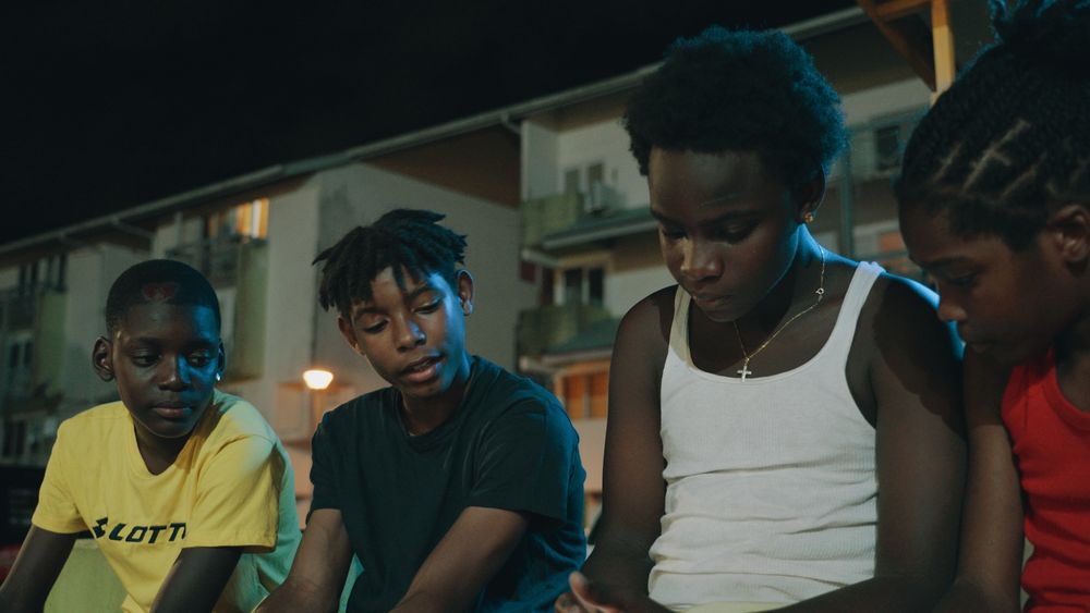 screen du film : trois enfants guyanais assis dehors en train de discuter, il fait nuit