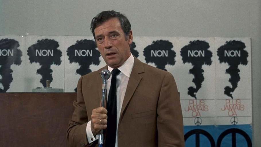 screen : Yves Montand en costume un micro à la main. Il parle, derrière lui des affiches avec de la fumée de bombe et écrit "non" dessus