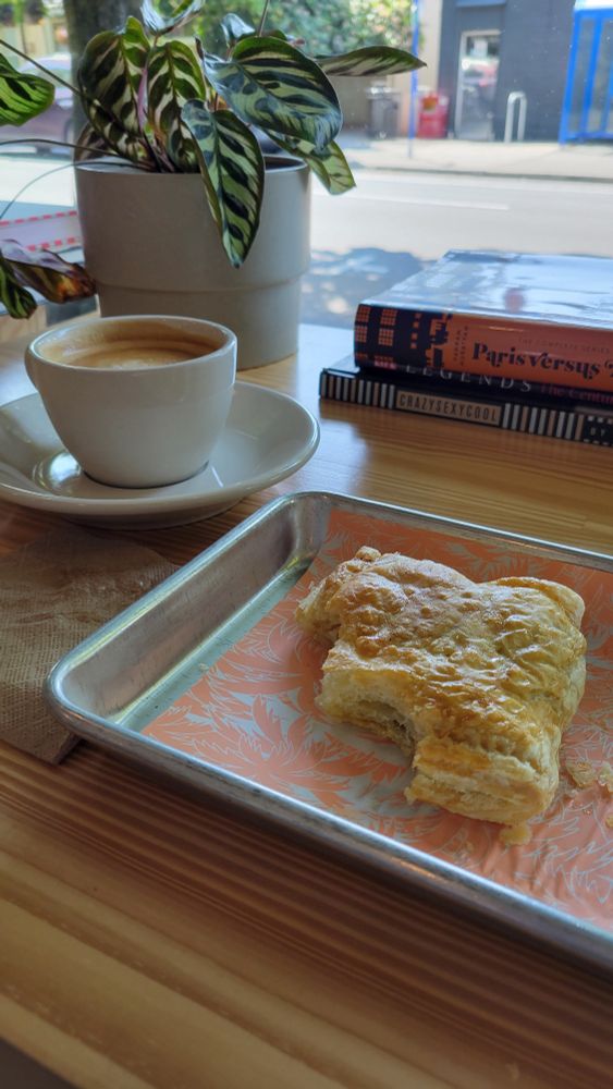 A potted plant and fresh pulled cortado at rear with a Marion berry (blackberry) and cheese pastry in foreground.