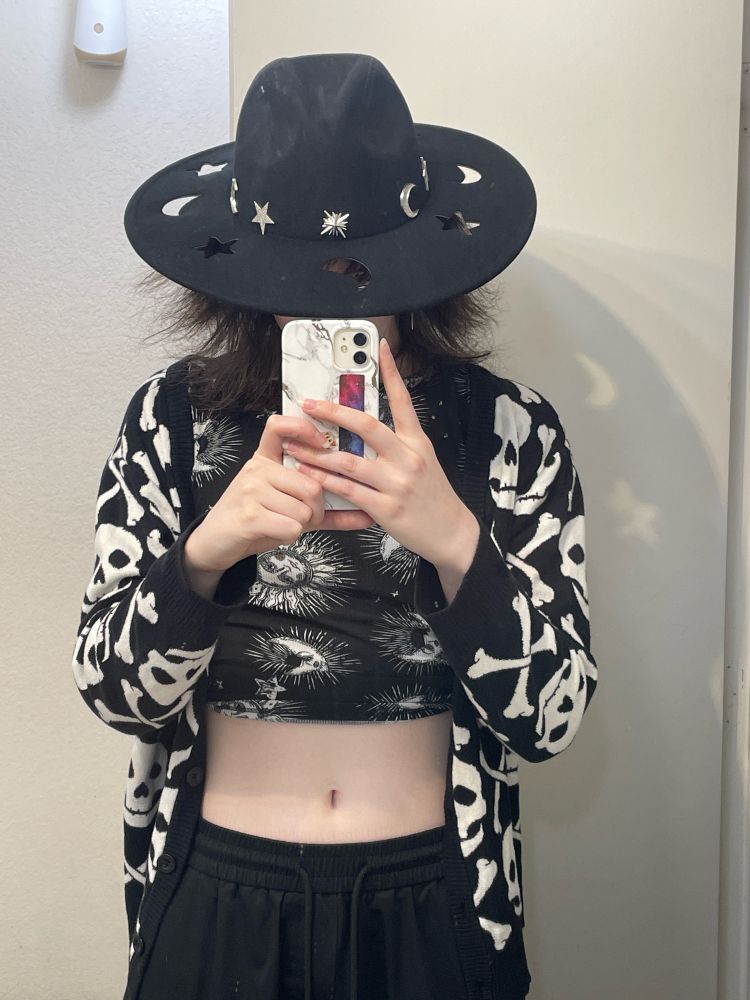 Me wearing black pants, a black and white sun and moon themed shirt with a black and white skull cardigan. Wearing a cowgirl hat with stars and moons cut out of the brim. 