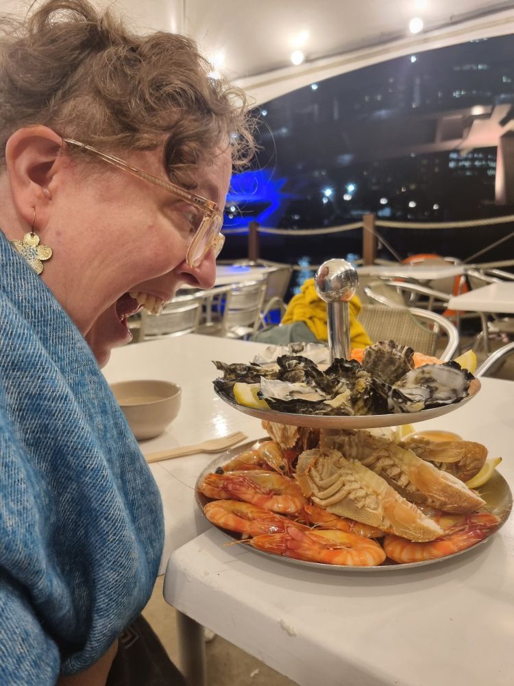 Distaff, a white woman, leaning in with a wide mouth to eat two levels of seafood.