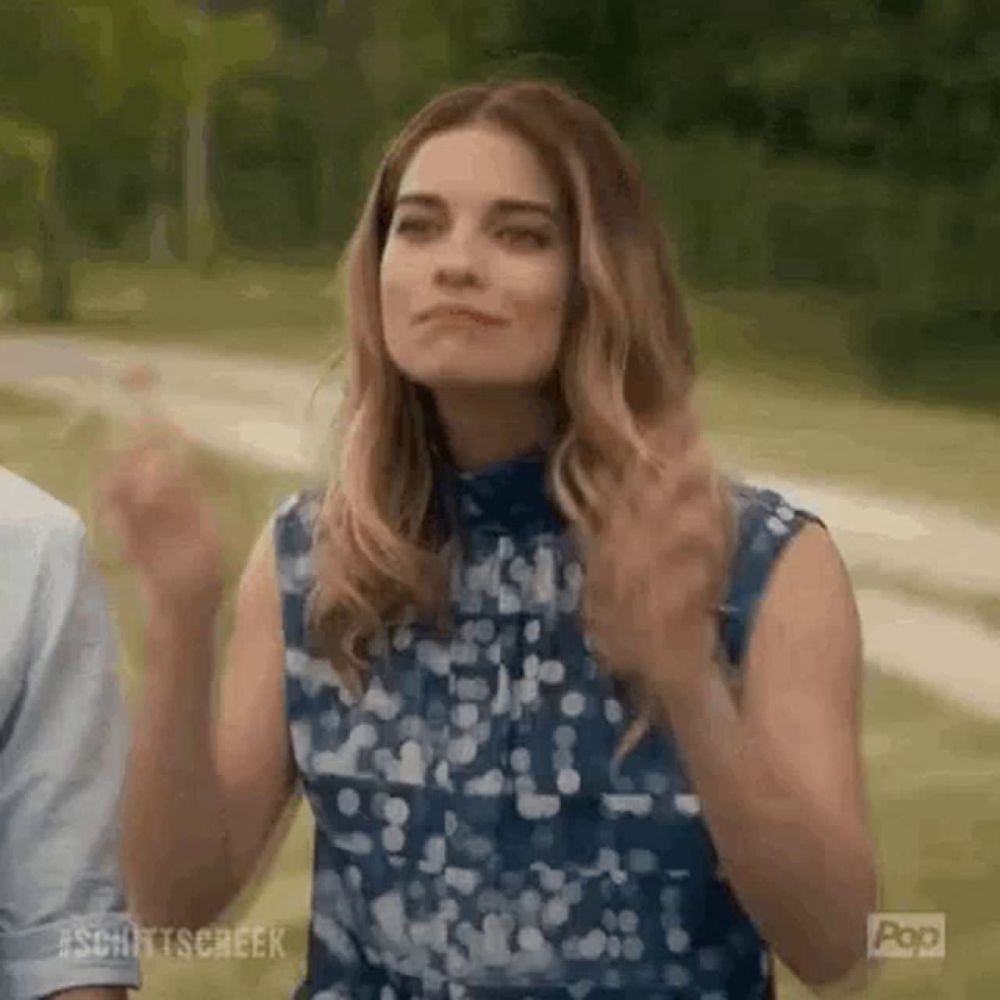 a woman in a blue dress is standing in a park with her hands in the air .