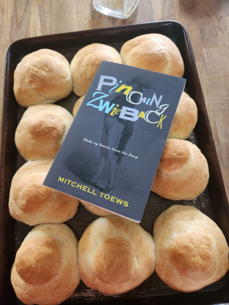 The highly-regarded book, Pinching Zwieback by Mitchell Toews is placed on a tray of hot Mennonite Zwieback buns.