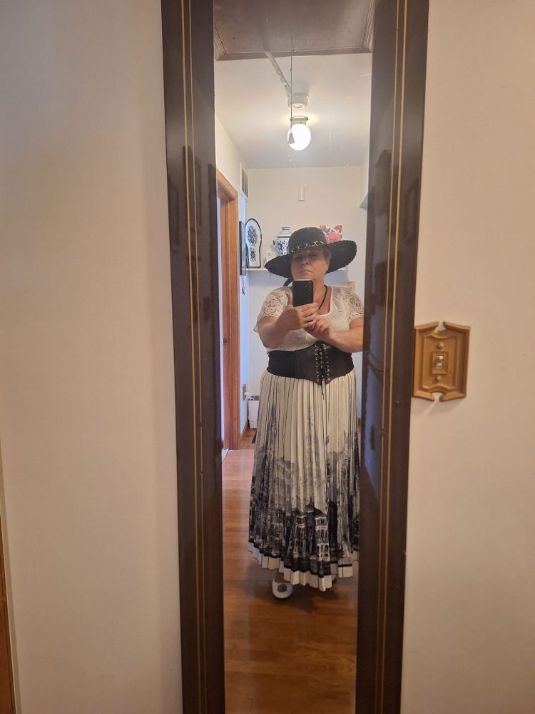 This image was taken in mirror-selfie mode for a favorite Niteflirt caller of mine, after he asked me what I was wearing out. It shows me wearing a black hat, a black and white bohemian-type outfit with a corset belt. White flat shoes. I am a mature BBW, full-figured woman in her 50s. I felt really pretty in that outfit. It is very much me! 