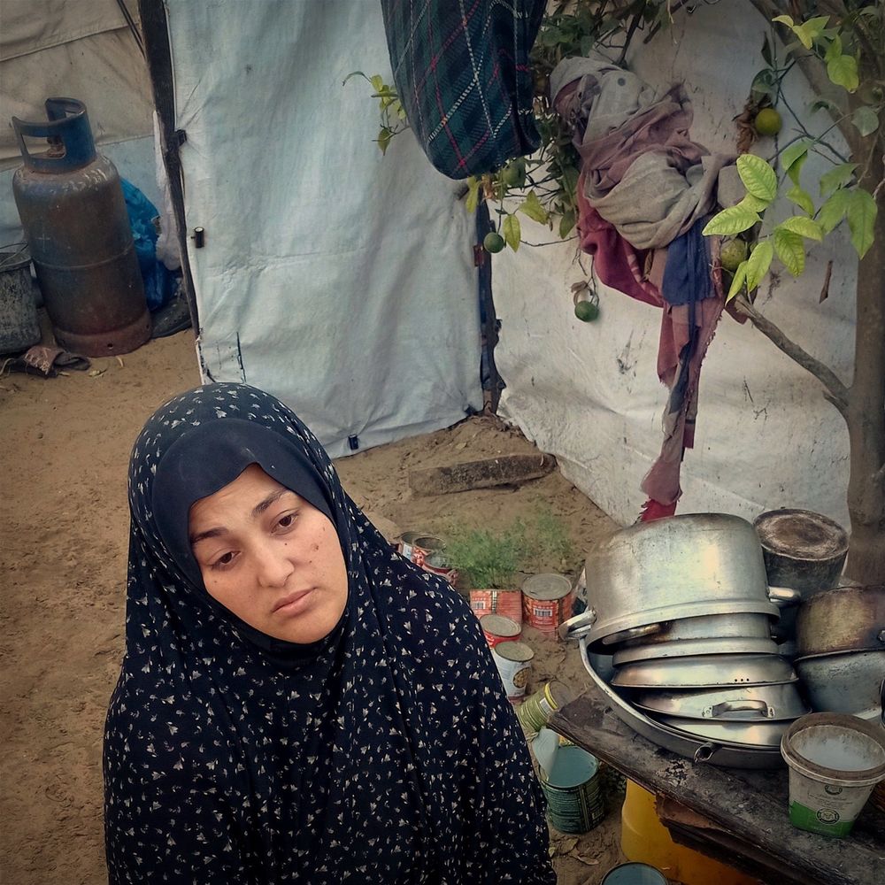 A photo of Abeer, a mother in G*za. Sitting in front of a tent while displacement in genocide. She looks very exhausted.
