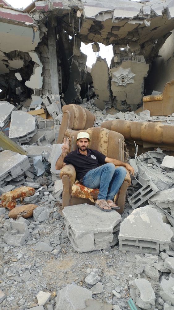 A photograph of Moutaz. He is sitting on an armchair surrounded by ruins and rubble.
The photo is taken while displacement and famine in ongoing genocide.
Gaza, Palestine.