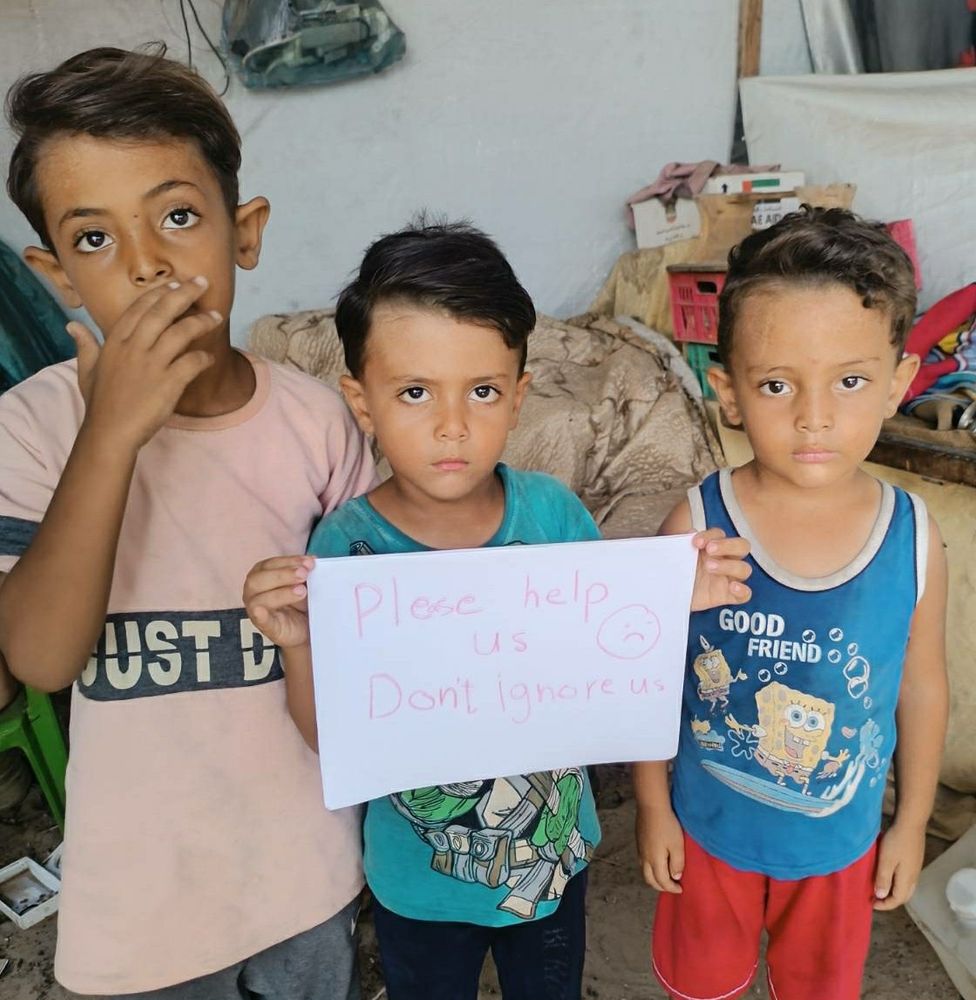 A photo of Eslam‘s three little sons: Eslam, Yahya and Mohamed
They are holding a sign: „Please help us.
Dont ignore us“

The photo is taken while displacement and famine in ongoing genocide. Gaza, Palestine.