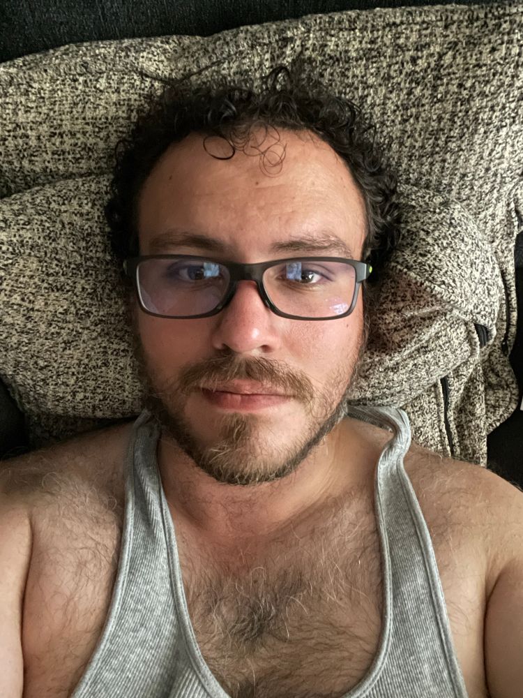 Me laying on my back with my work glasses on and a gray tank top. Chest hair prominently on display. 