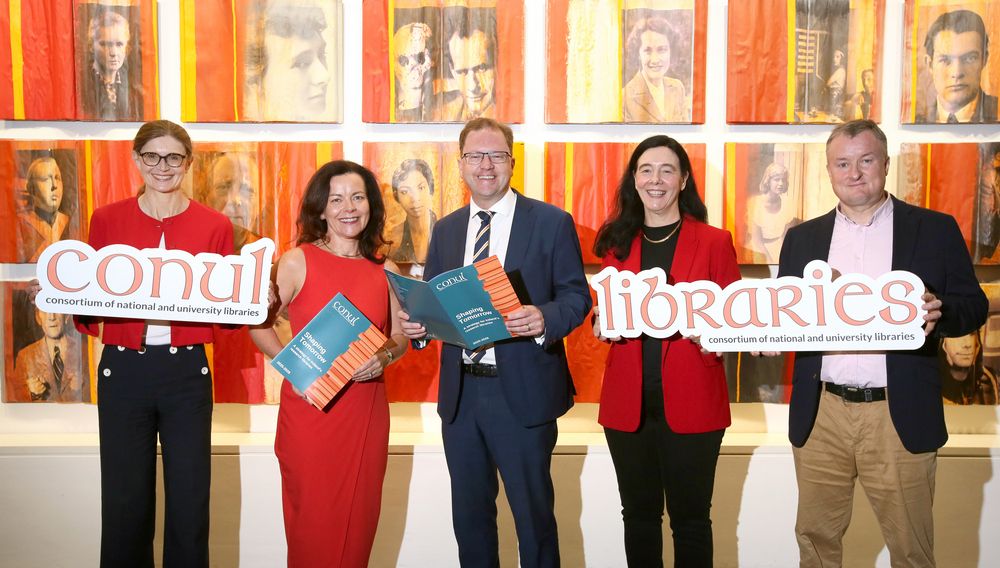 Five people, three women & two men holding CONUL strategy documents and smiling for the camera. The women are all wearing red, and the men both wearing navy blazers.