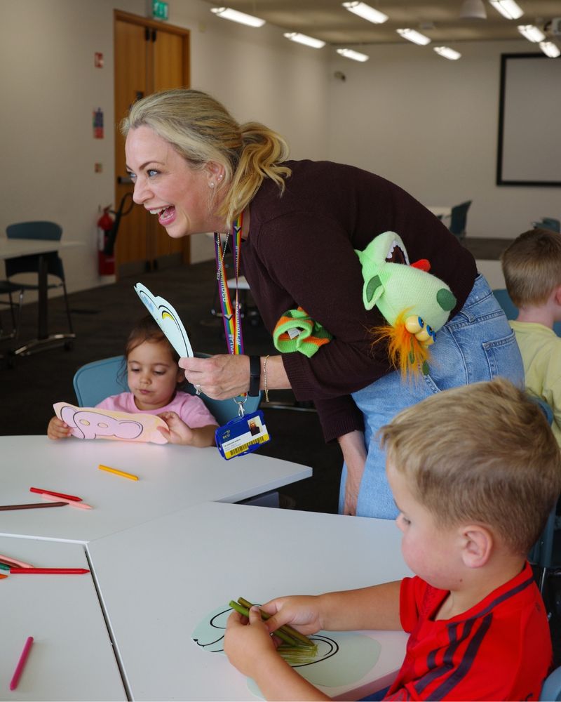 Children with crayons and elephant colouring pages and a laughing woman with a colourful pupper under her arm