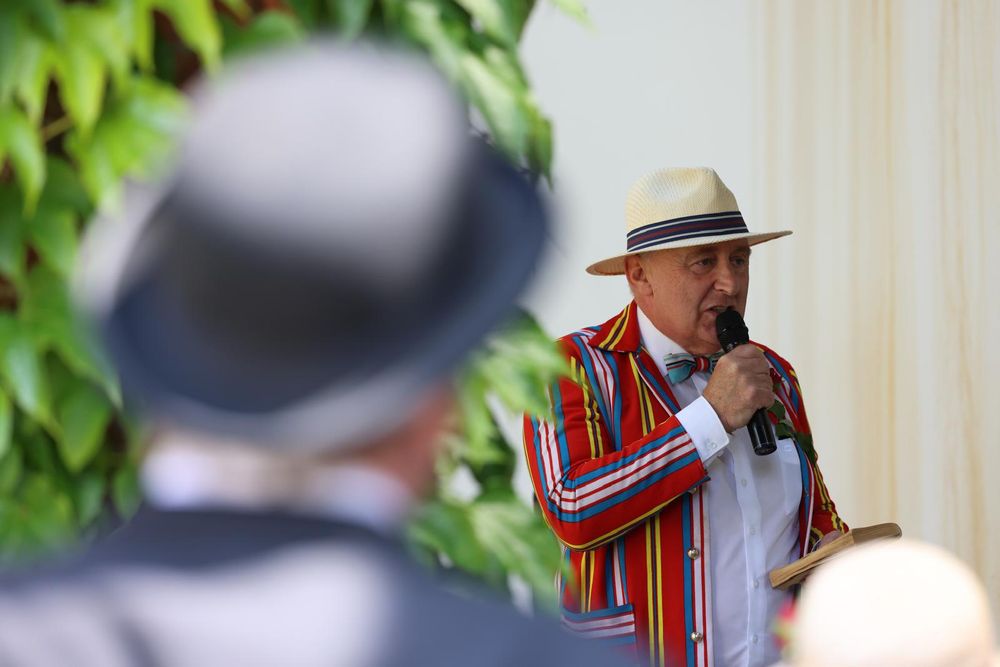 A man with a hat and striped jacket speaking into a microphone
