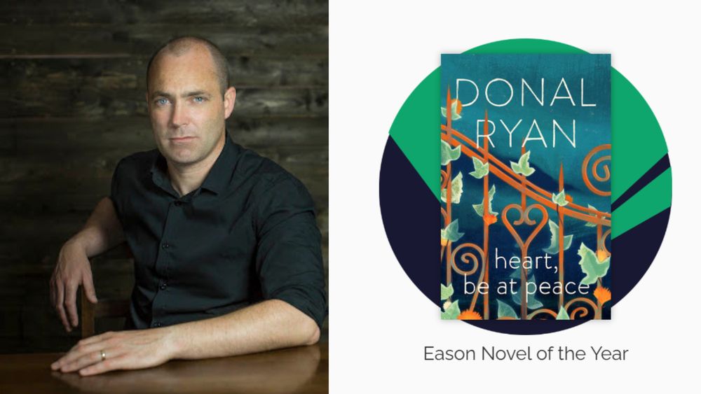 A man sitting at a table, facing the camera beside a picture of Heart be at peace by Donal Ryan - Eason Novel of the Year.