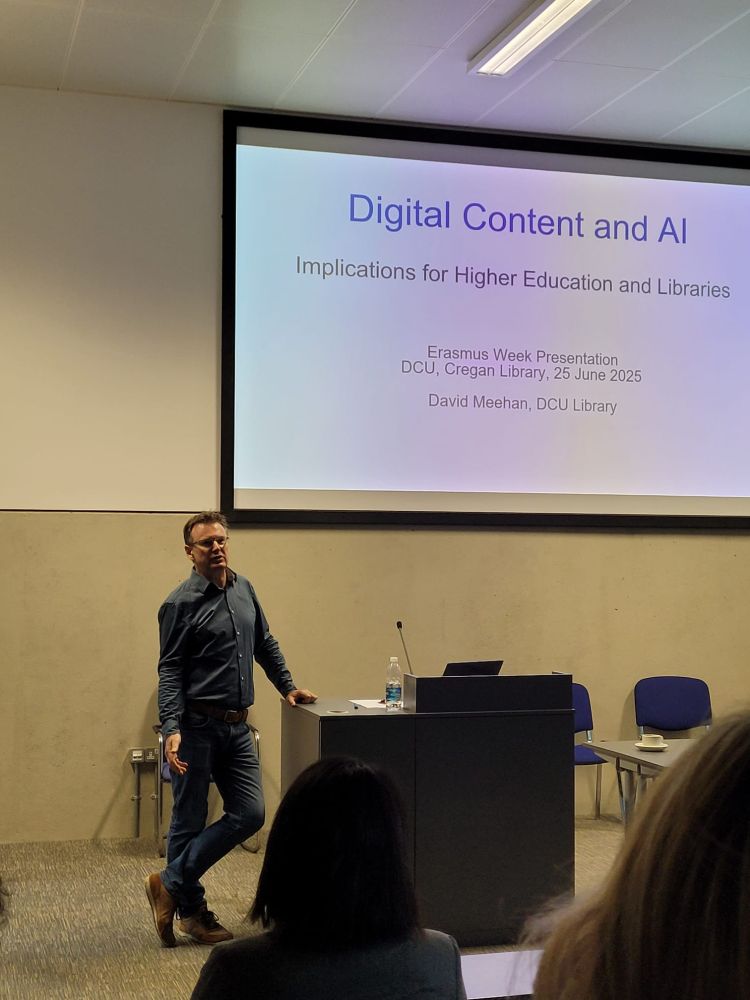 A man standing beside a lectern, in front of a projector screen that reads 'Digital content and AI.'