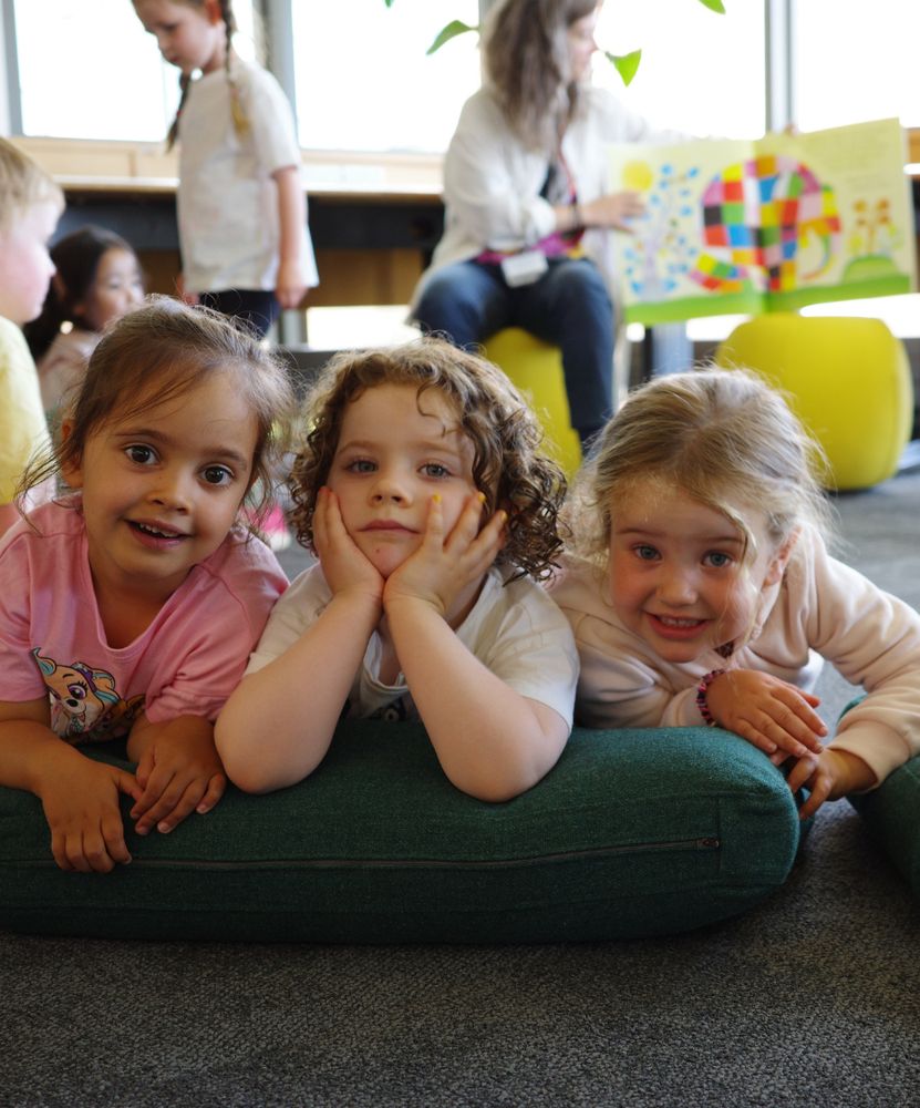 3 small children leaning on their elbows smiling at the camera