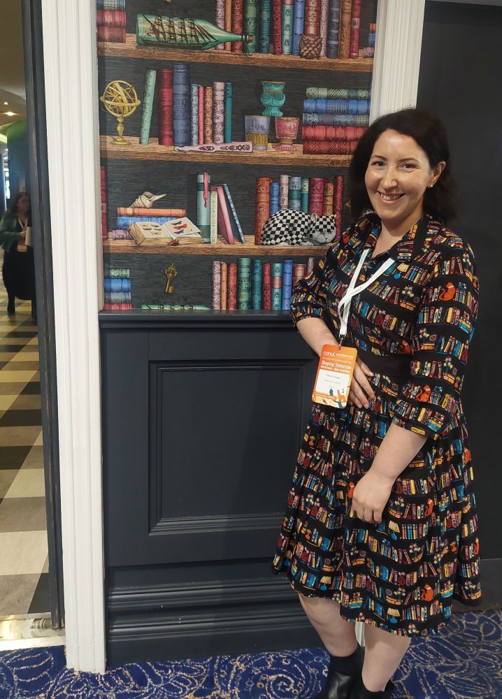 A woman in a library print dress standing in front of book wallpaper 