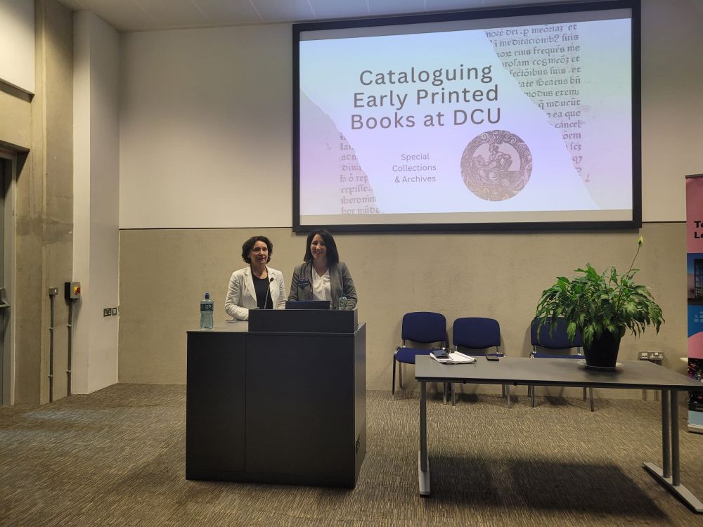 Two women standing beside a lectern in front of a screen that reads Cataloguing Early Printed Books at DCU
