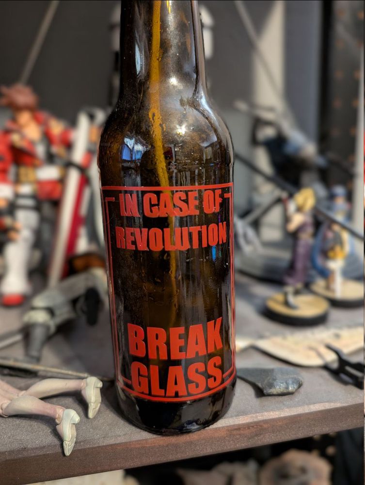 A glass bottle with a minimalist industrial design in red vinyl that reads In Case of Revolution Break Glass. 