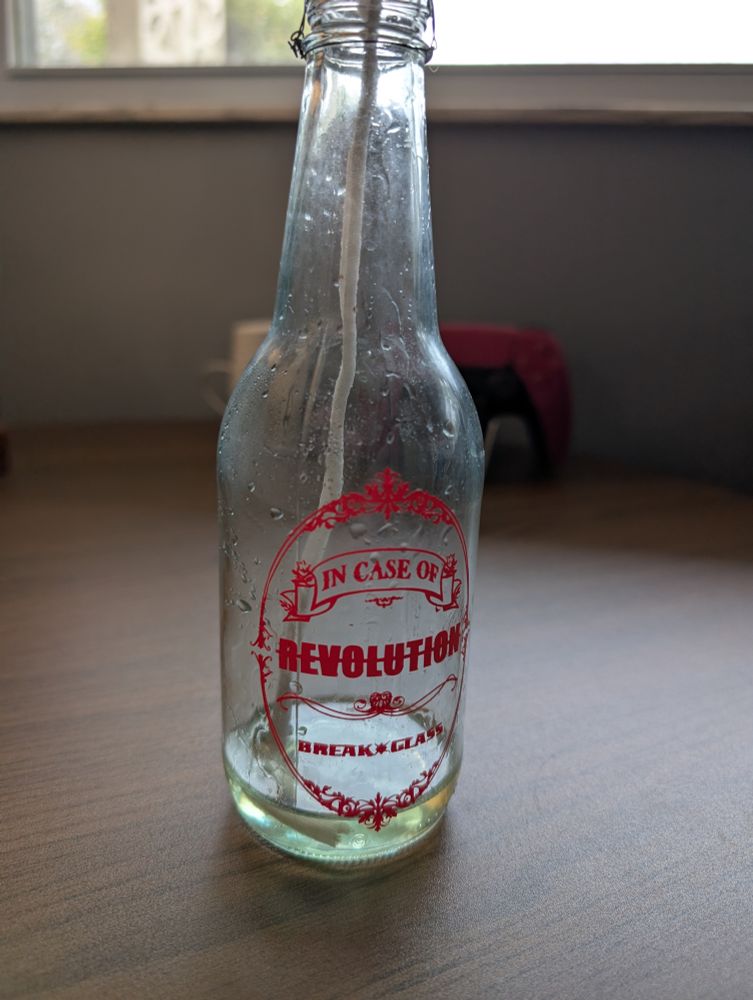 A glass bottle with a filigree design in red vinyl that reads In Case of Revolution Break Glass. 