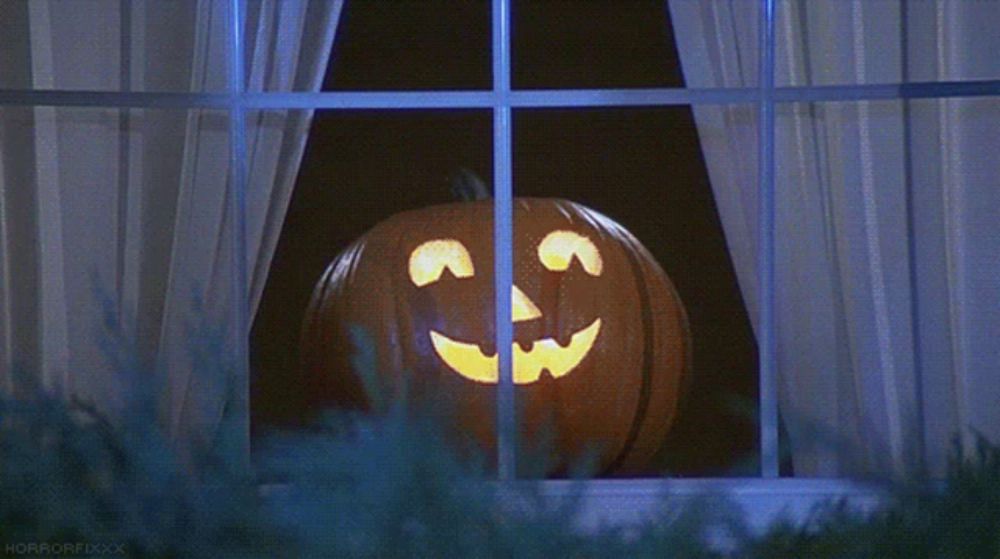 a pumpkin with a face carved into it looks out a window