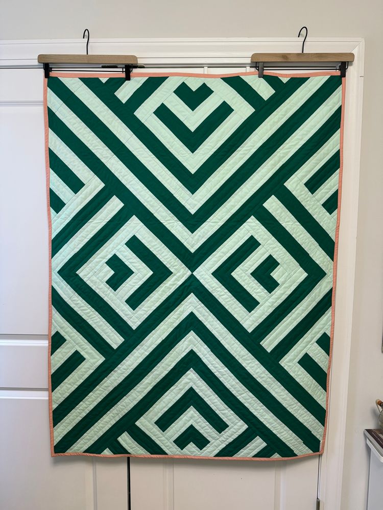 Photo of a handmade geometric quilt in two shades of green with a pink border. 